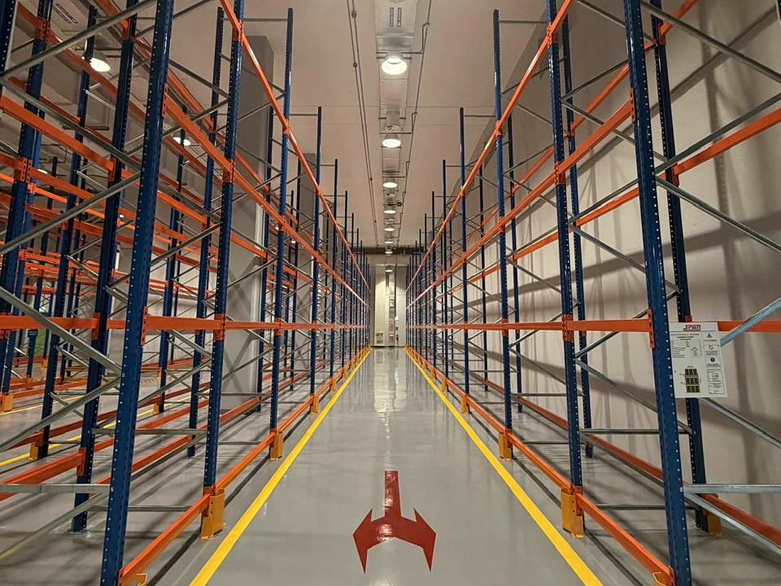 High-bay warehouse racking aisle with lighting and floor marking, services delivered by Mecamac
